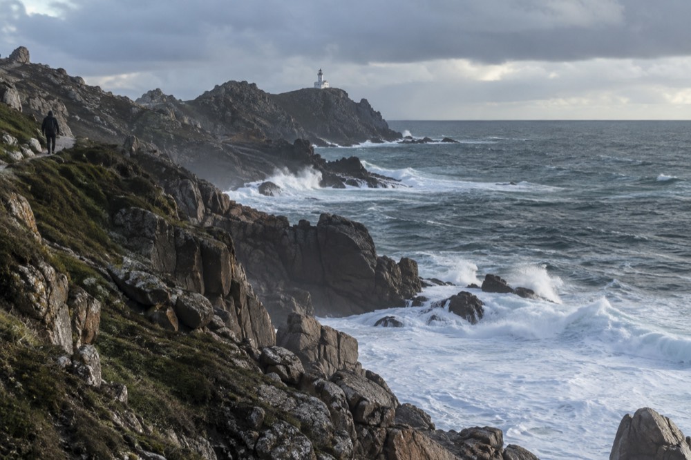 Waves breaking against dark granite rocks below a cliff path on the Costa da Morte