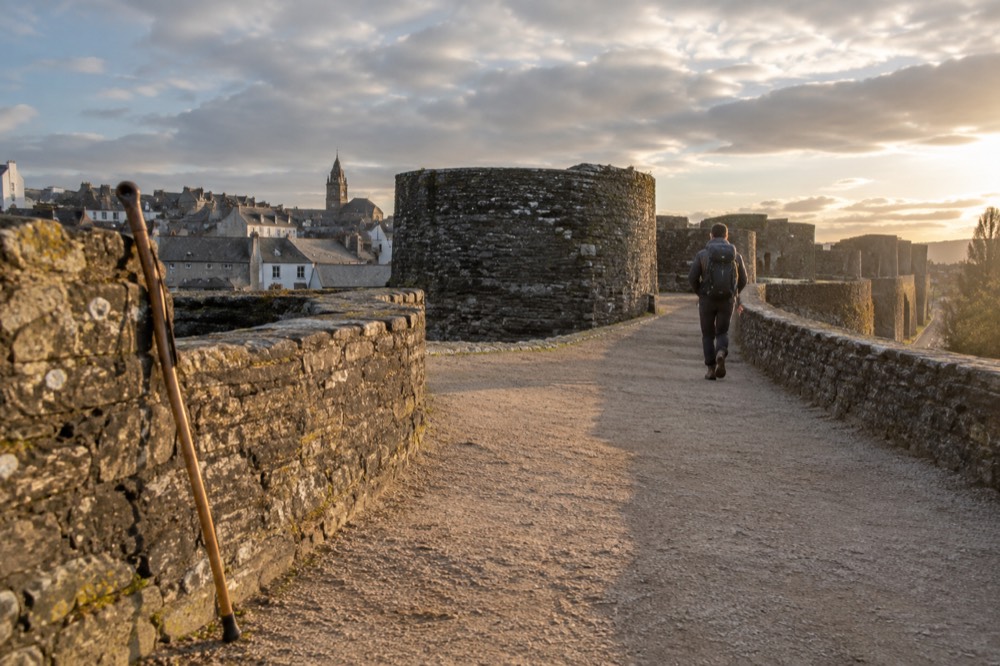 A pilgrim walking stick resting against the stone walls of Lugo at golden hour