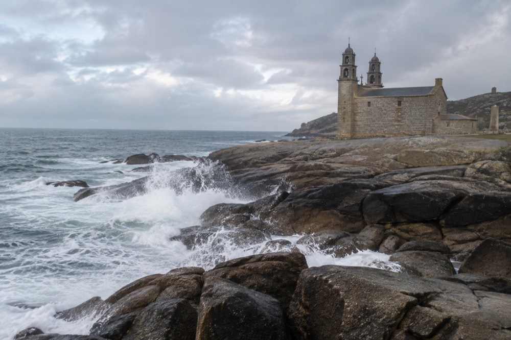 A granite sanctuary church beside the ocean with waves breaking on dark rocks in the foreground
