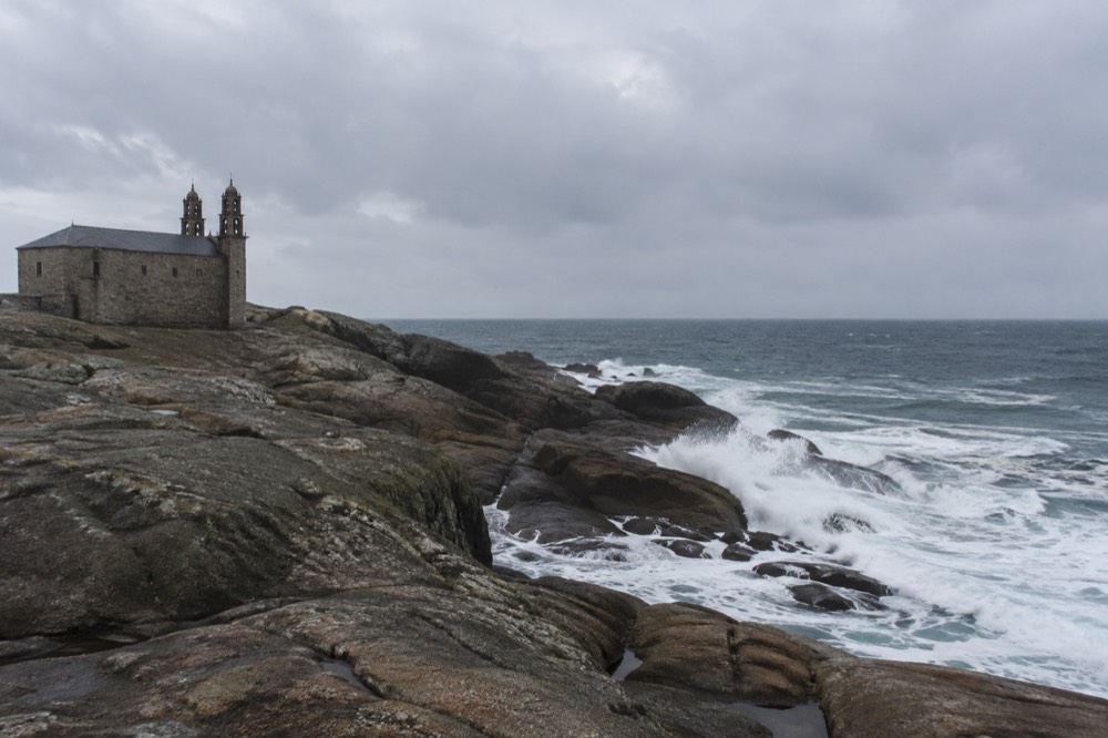 Waves breaking against dark coastal rocks with white spray under a grey Atlantic sky