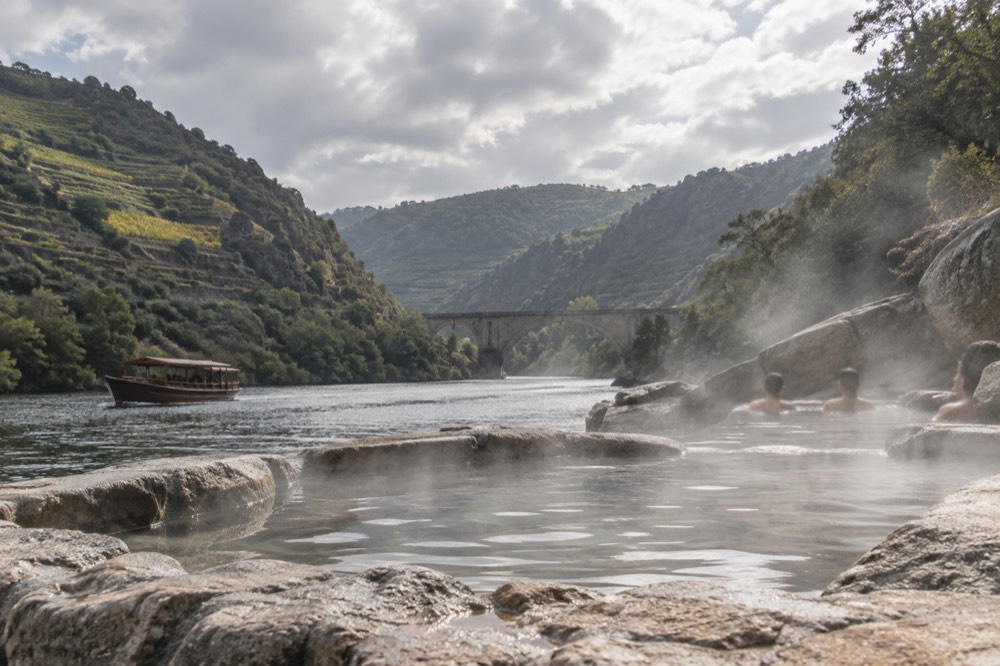 A wooden river boat cruising between steep canyon walls with terraced vineyards on the slopes above