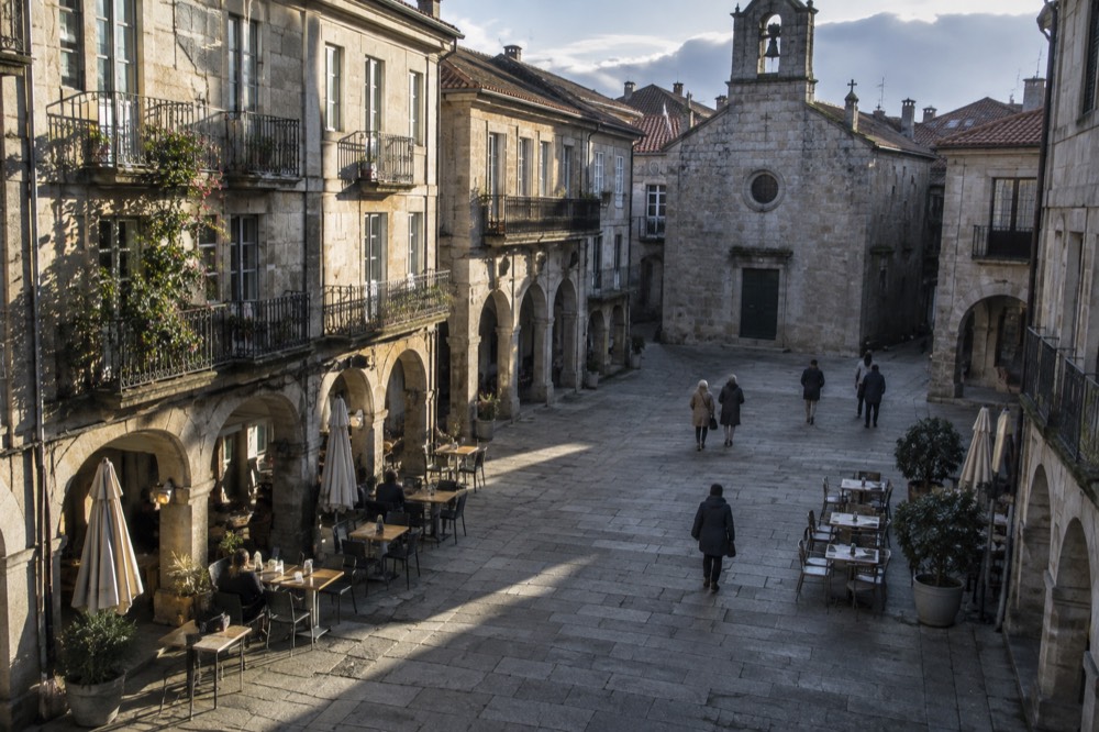 Granite arcade square in Pontevedra with cafe tables under stone arches on a sunny morning