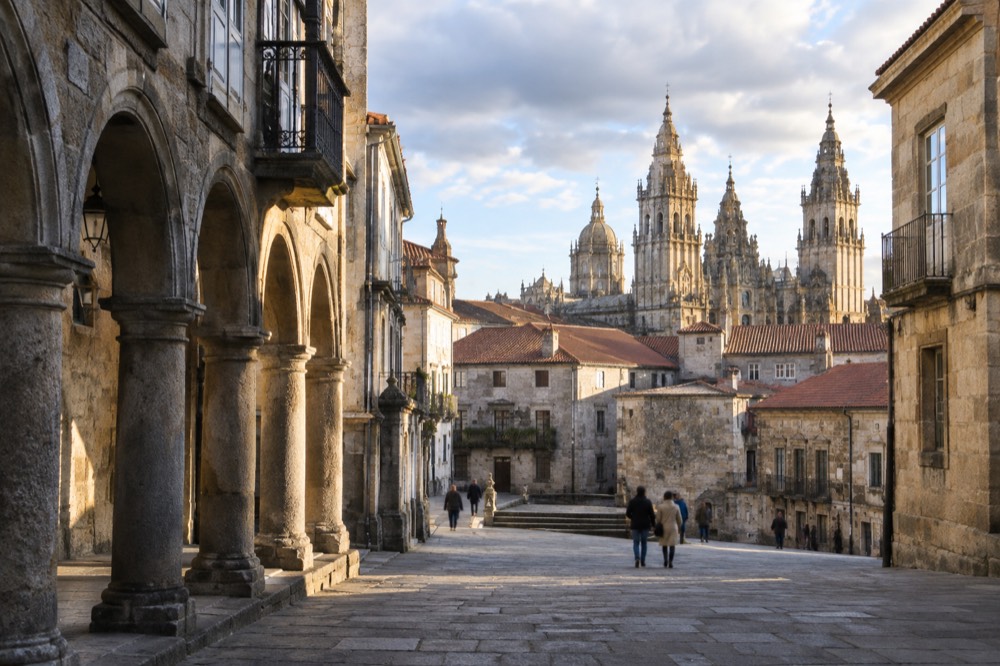 Wide view of a Galician old town at golden hour with stone towers and terracotta rooftops