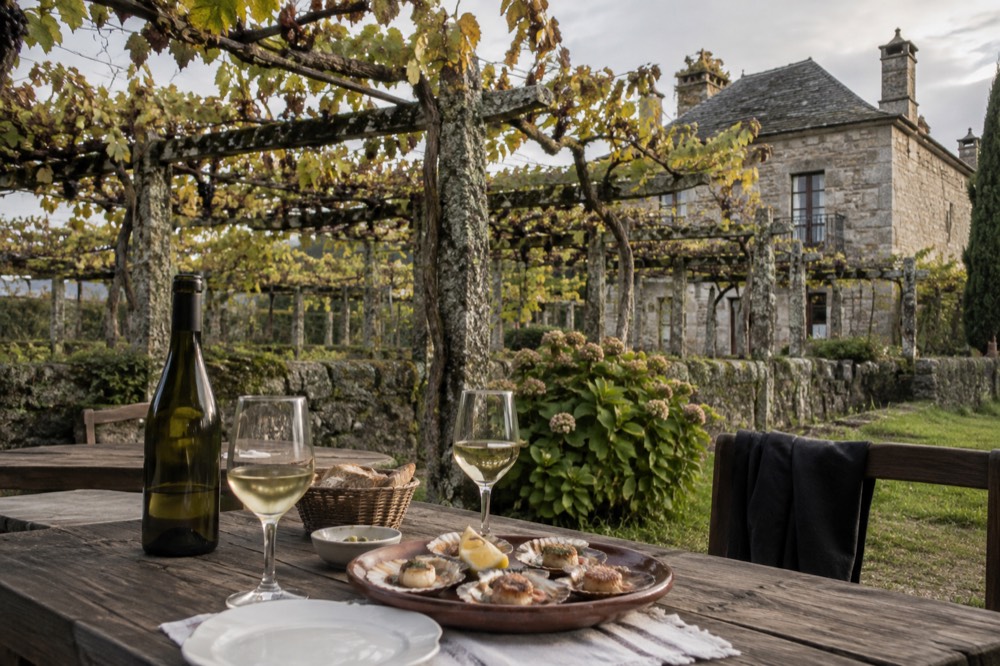 A wooden table with a bottle of Albariño, glasses and a plate of grilled scallops in a stone-walled restaurant