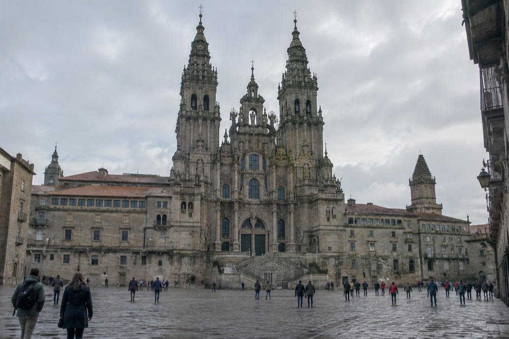 A tall stone cathedral interior with ornate golden altar and large crowds of visitors below a dome
