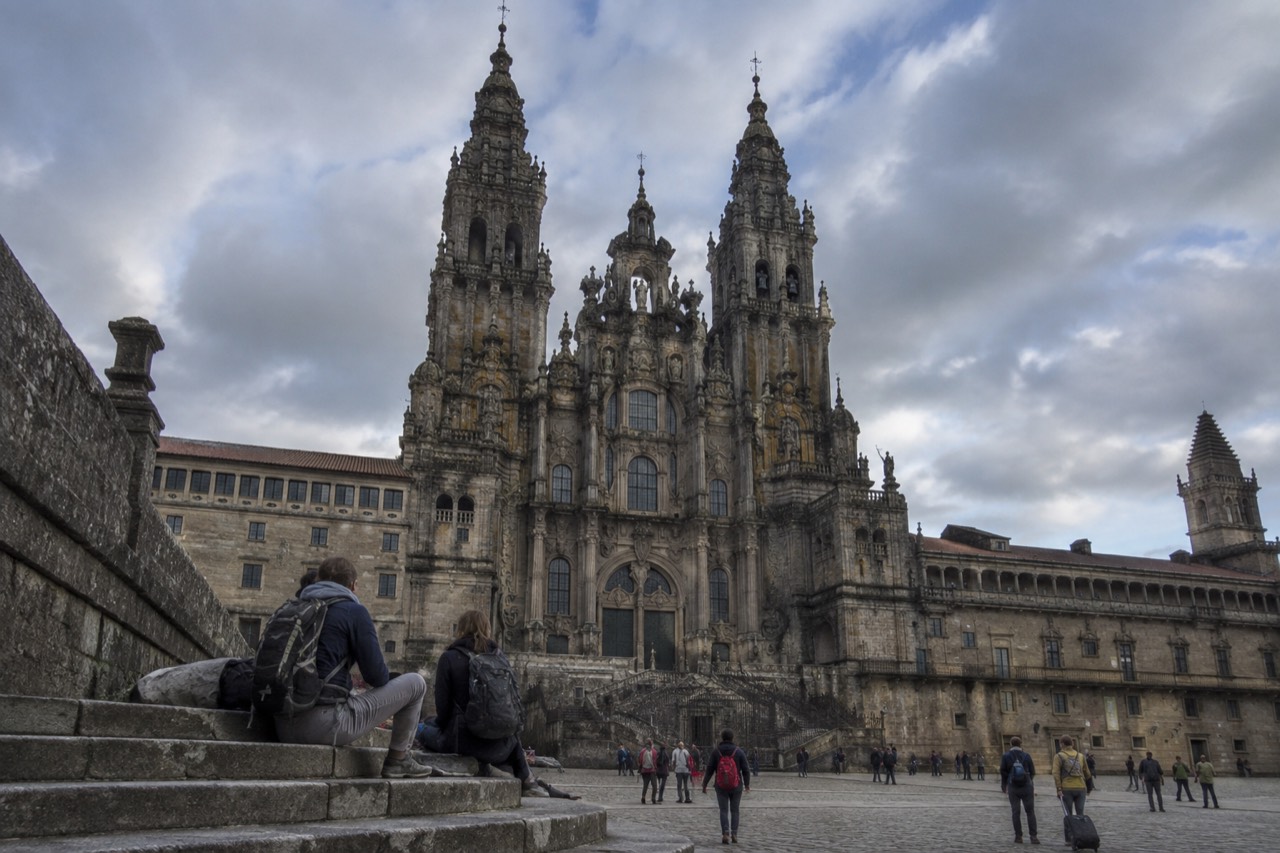 Pilgrims with backpacks resting on stone steps near a historic building in Santiago de Compostela