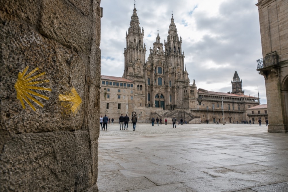 Yellow Camino route arrow and scallop shell marker on a stone wall in a Galician village