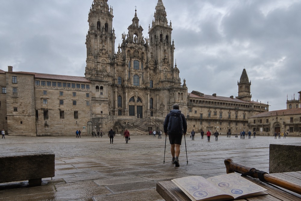 A pilgrim passport with collected stamps spread on a wooden table beside a walking stick
