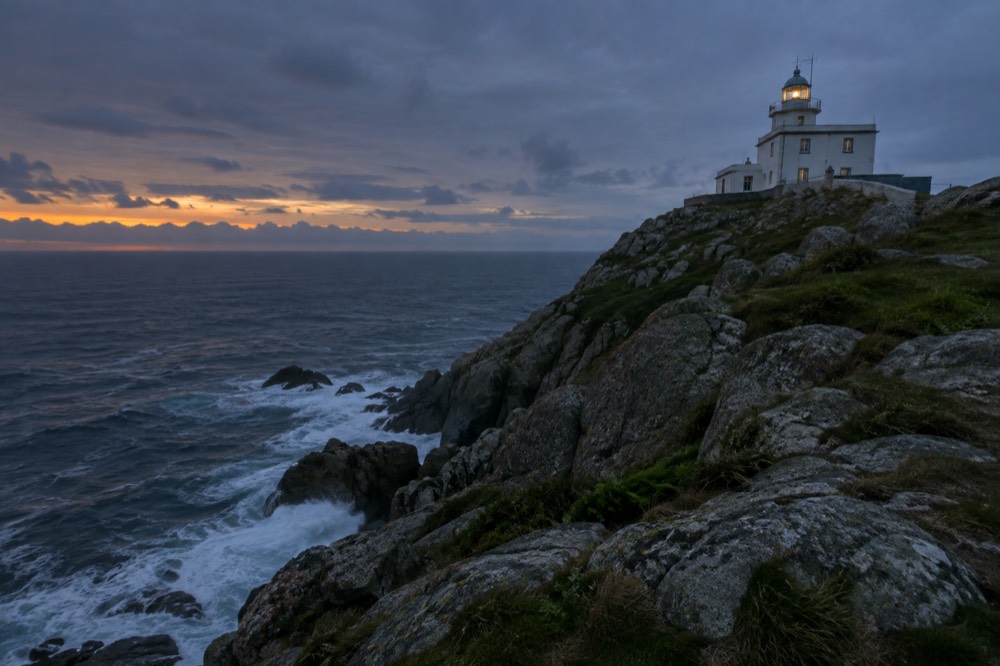 Waves breaking against the rocky lighthouse point at Fisterra on the Costa da Morte at sunset