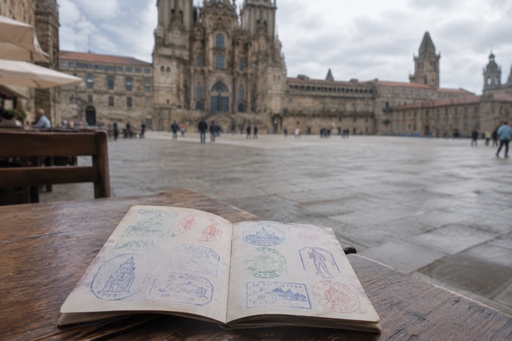 A pilgrim passport lying open on a wooden table showing several colorful ink stamps
