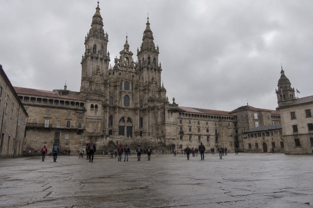 A line of pilgrims walking beside a rural stone wall under an overcast sky in northern Spain