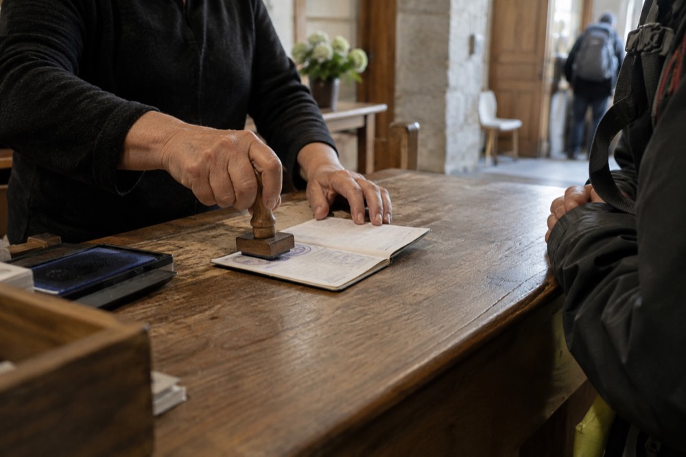 A pilgrim's credential passport being stamped at a wooden counter in an albergue