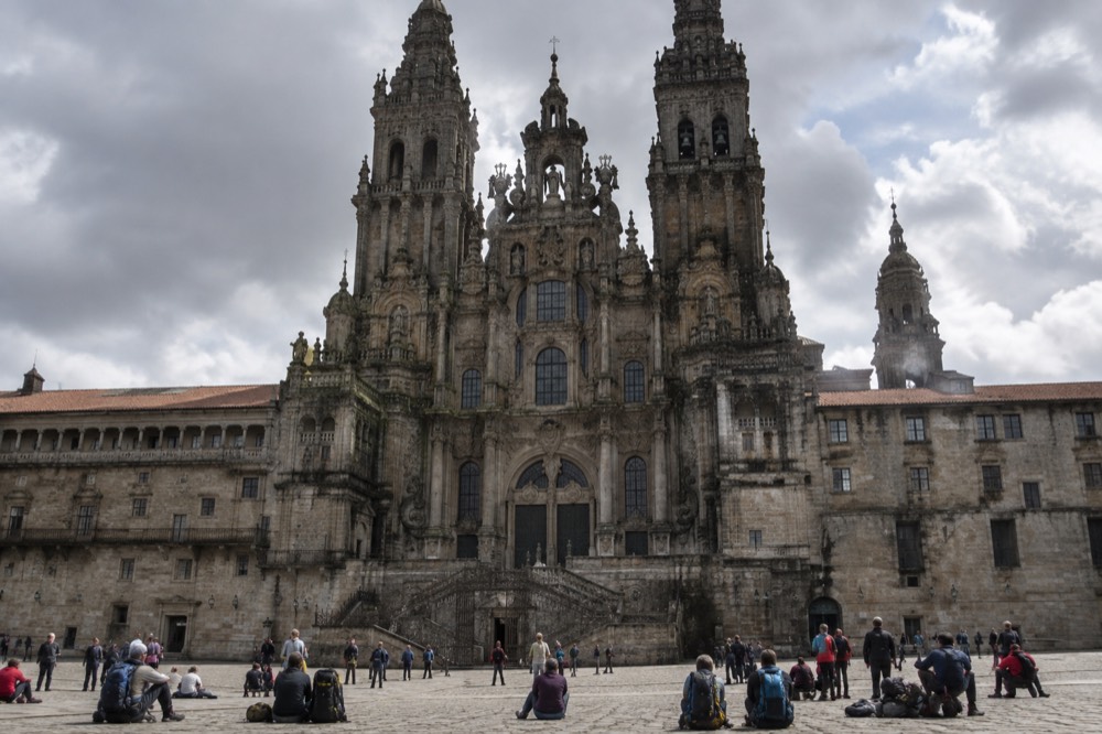Pilgrims resting with backpacks on the stone pavement of a large square facing a baroque cathedral facade