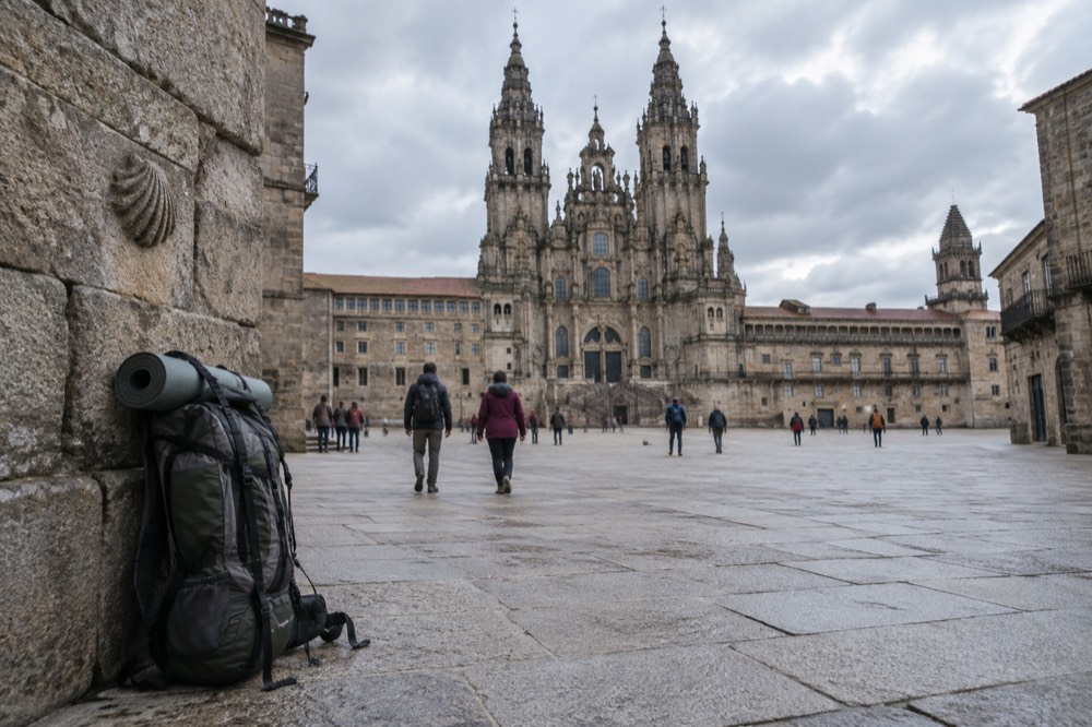 A loaded backpack resting against a stone wall beside scallop shell markers