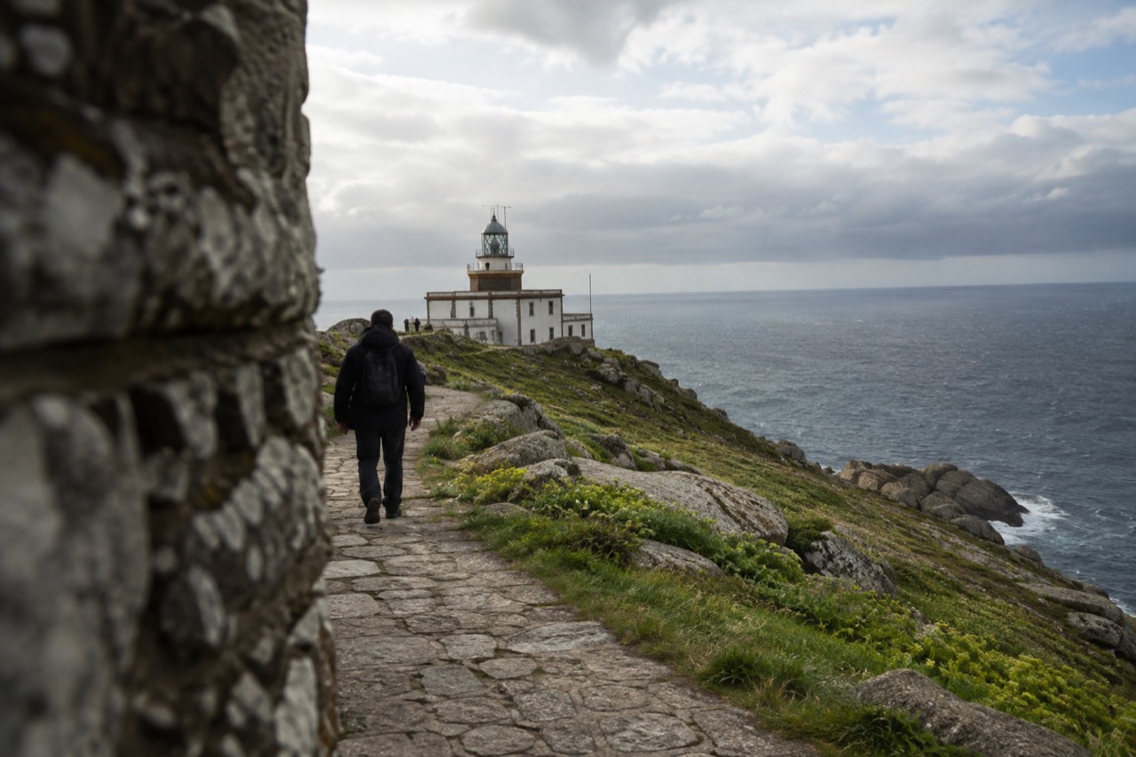 A stone path winding through green Galician countryside toward the Atlantic coast at Fisterra