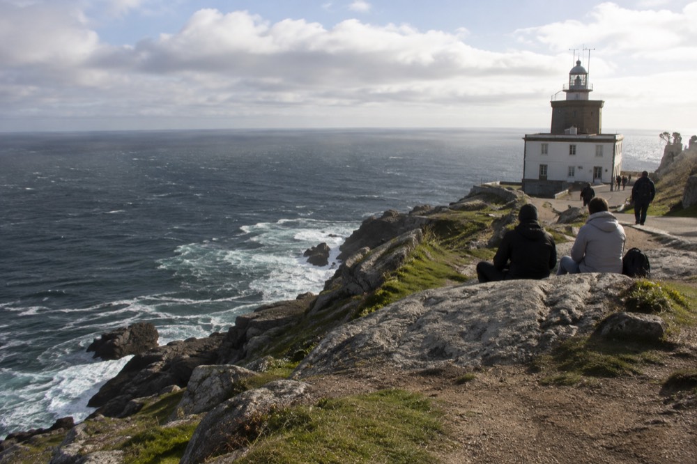 Walkers resting on a cliff path above the Atlantic near Fisterra lighthouse