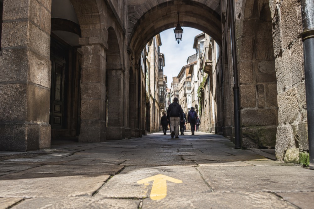 A stone archway on an old town street in northern Spain with a yellow Camino arrow painted on the paving