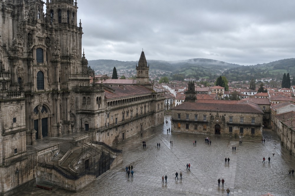 A green rolling landscape with a stone village and mist under a grey sky in rural Galicia