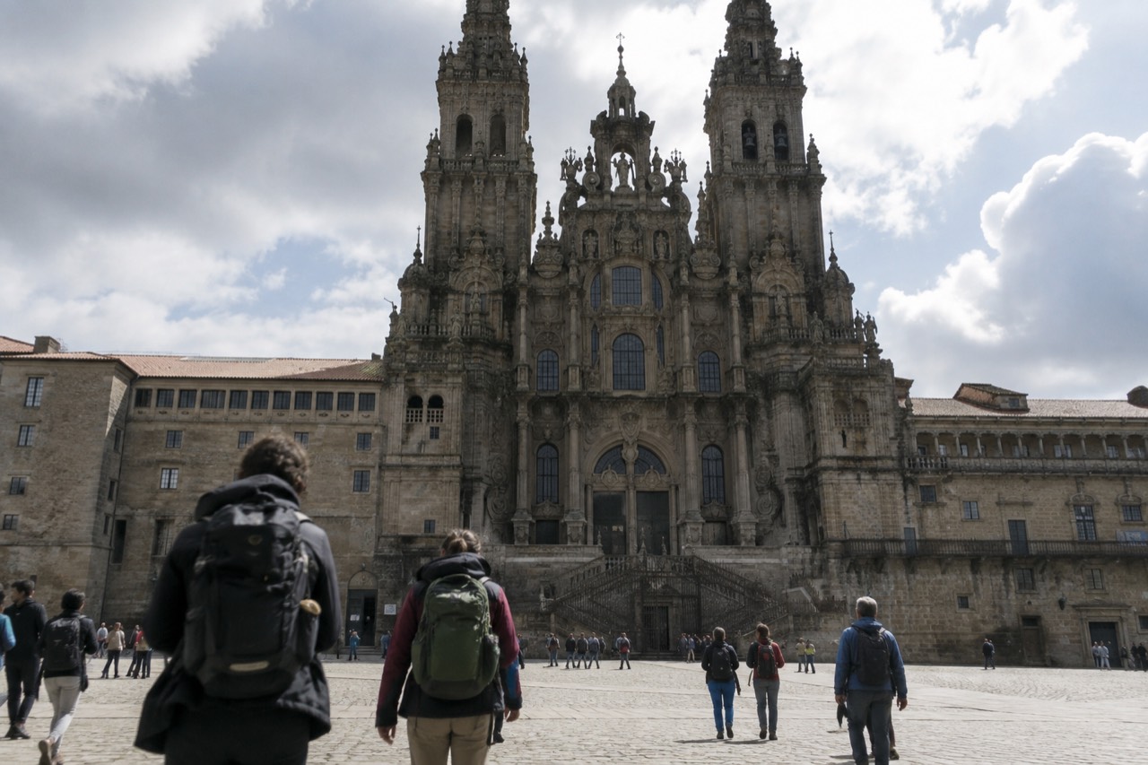 Pilgrims with backpacks walking a green wooded path in rural Galicia on their way to Santiago de Compostela