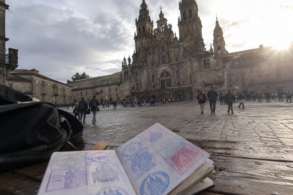 A pilgrim passport booklet open on a wooden table showing square ink stamps