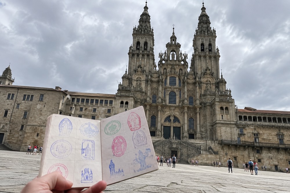 A pilgrim passport held open showing colorful ink stamps collected along the route