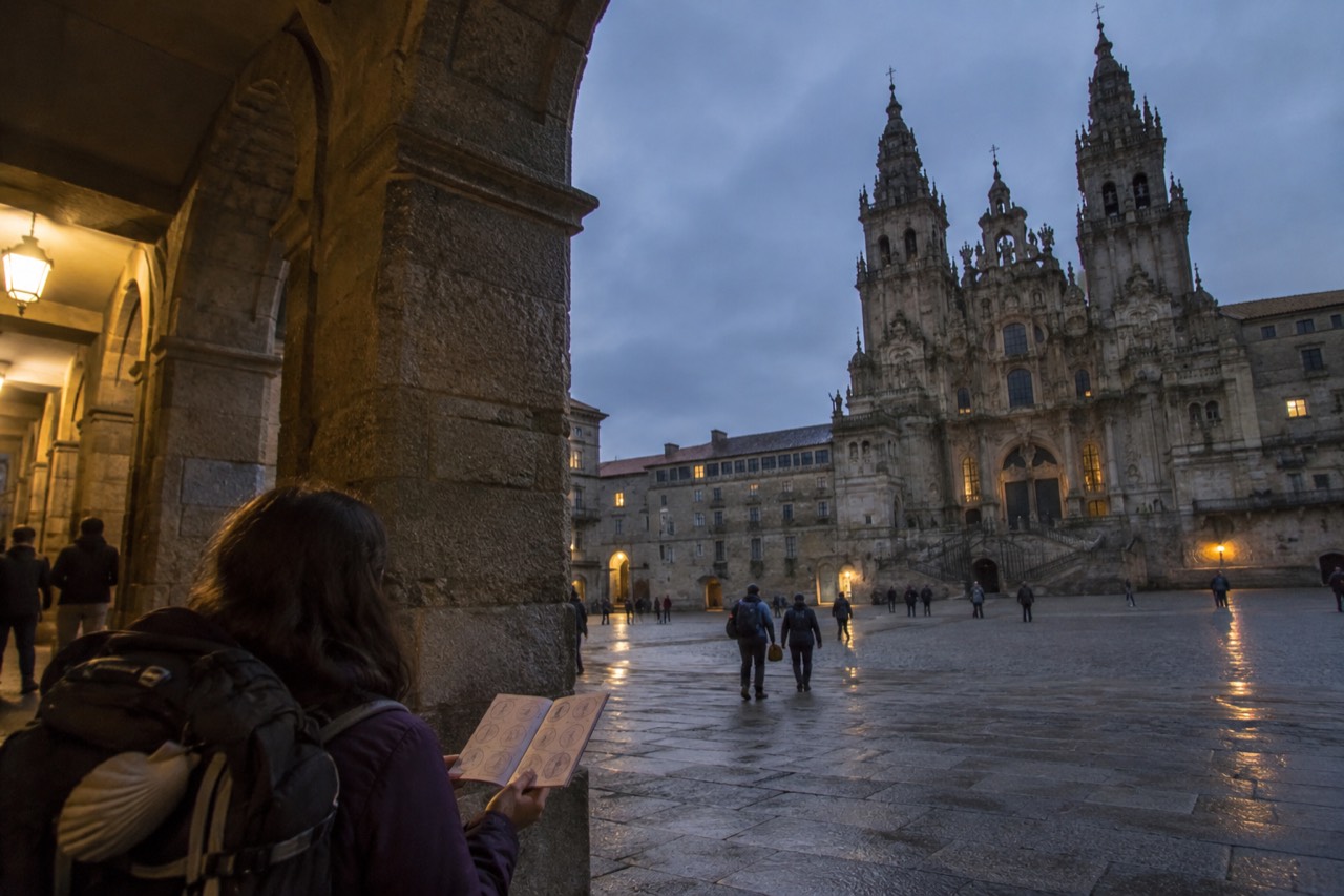 Pilgrims holding stamped credential documents in a stone arcade near the cathedral