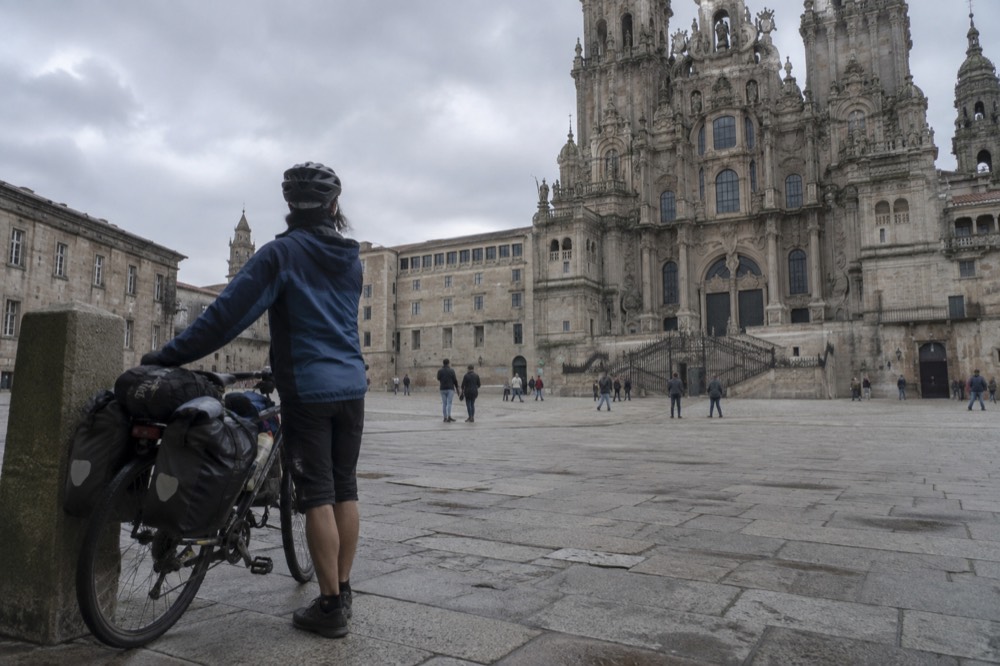 A cyclist leaning on a loaded touring bike beside a stone Camino marker