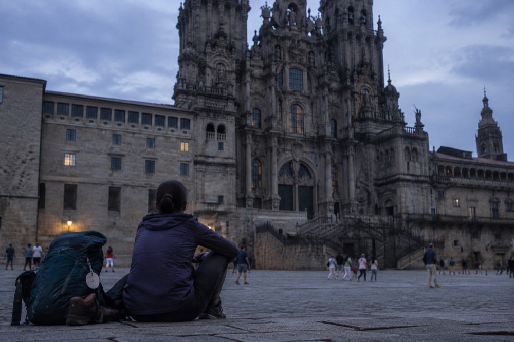A pilgrim in hiking gear resting with a backpack near the baroque facade of Santiago de Compostela Cathedral