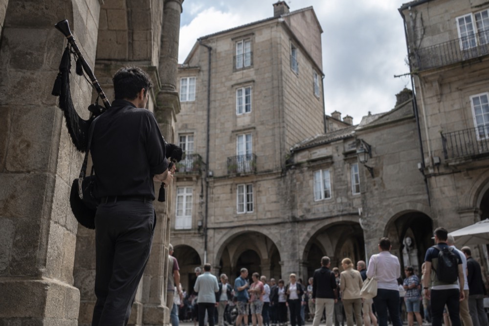 A street musician playing bagpipes for a summer crowd in a granite arcaded square in Santiago de Compostela