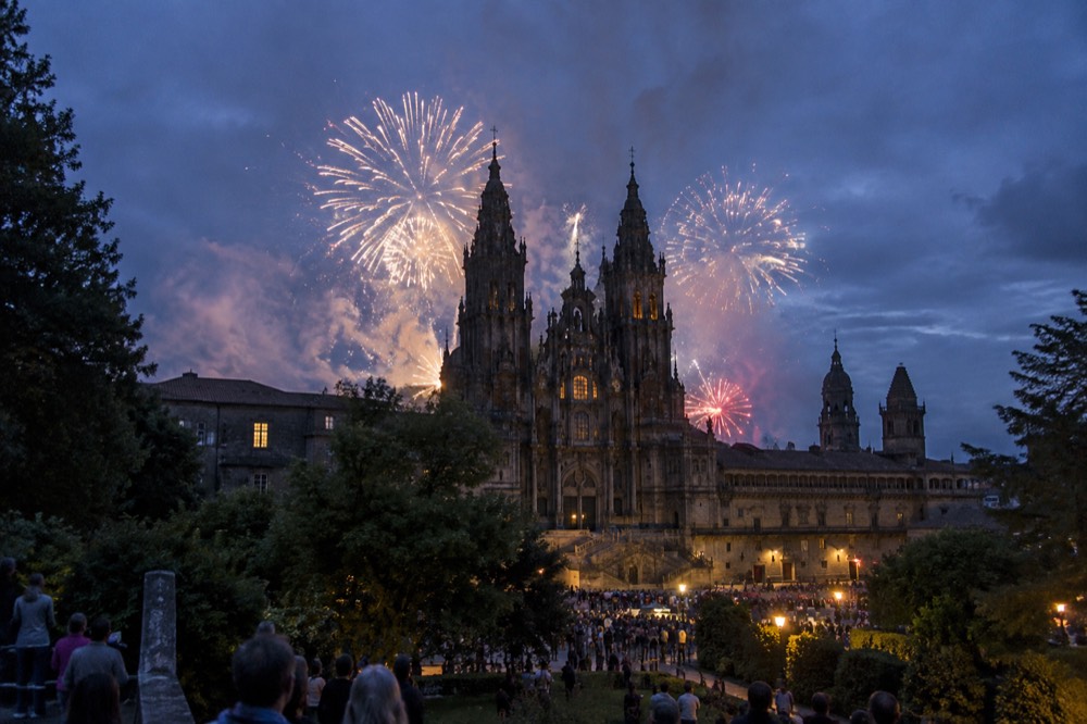 Fireworks bursting over the towers of Santiago de Compostela Cathedral seen from a park at night