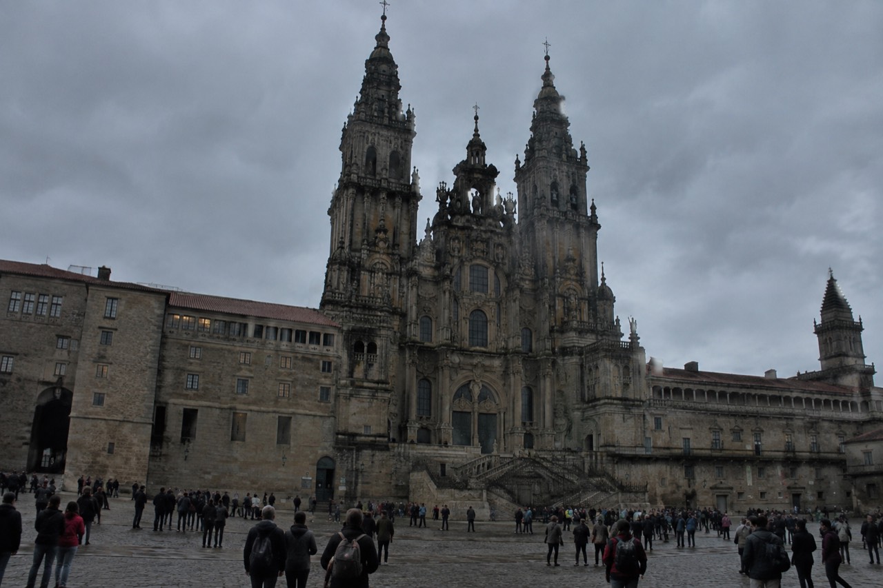 Crowds gathered in a granite square in front of a baroque cathedral at dusk