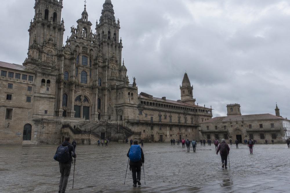 Pilgrims arriving in Praza do Obradoiro with backpacks and walking staffs