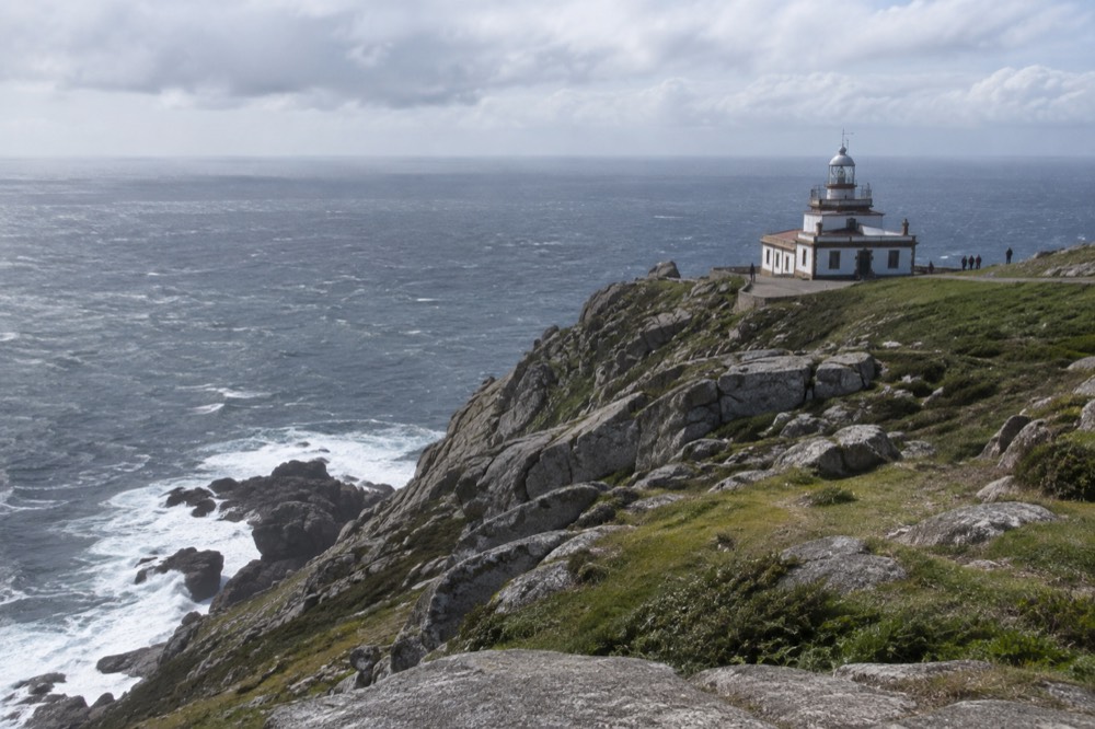 A lighthouse on rocky Atlantic cliffs at Fisterra with waves breaking below