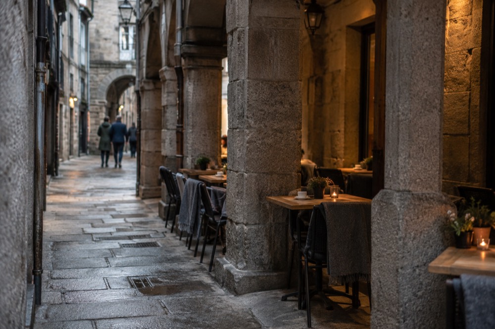 A narrow stone street in the old town with restaurant tables set out under a covered arcade in the evening