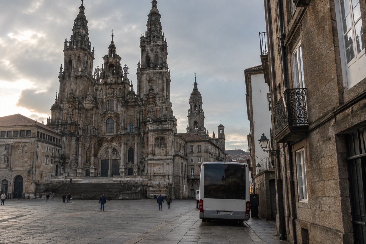 A city bus parked on a narrow stone street beside old granite buildings in Santiago de Compostela