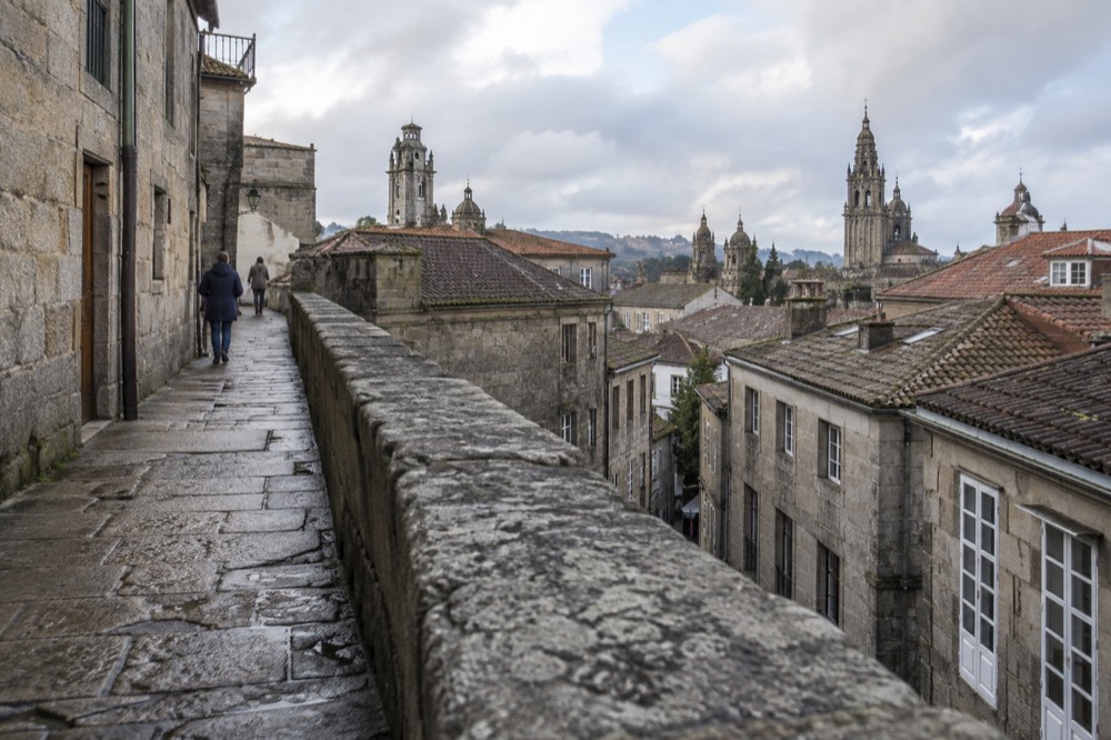 A stone rooftop walkway with views over the rooftops and towers of a historic city