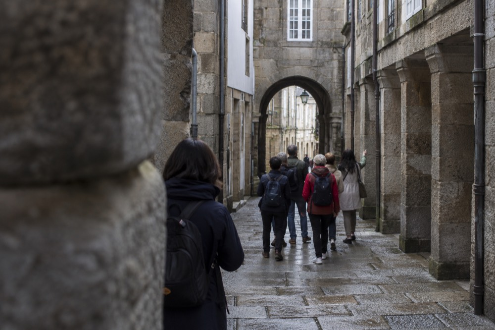 A walking guide showing a small group of visitors a stone archway in the old town of Santiago de Compostela