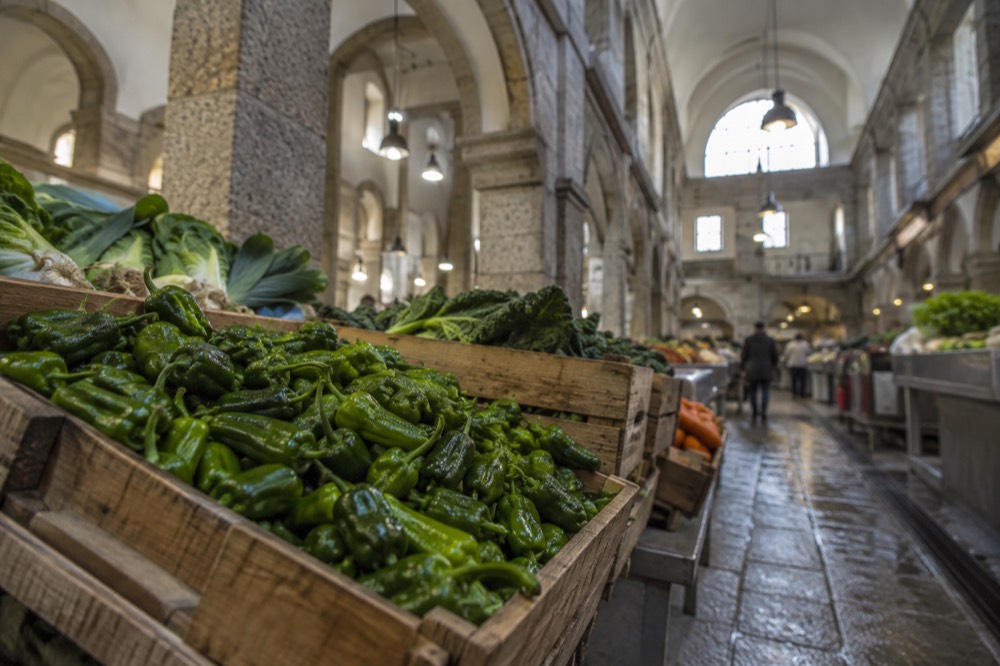 A market stall display of small fresh green peppers in wooden crates