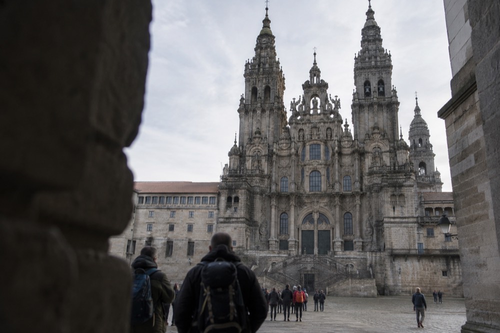 Walkers with backpacks standing in a side aisle of Santiago de Compostela Cathedral during a service
