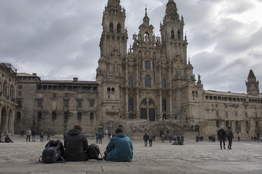 Pilgrims resting on the stone floor of Praza do Obradoiro with the Cathedral facade behind them