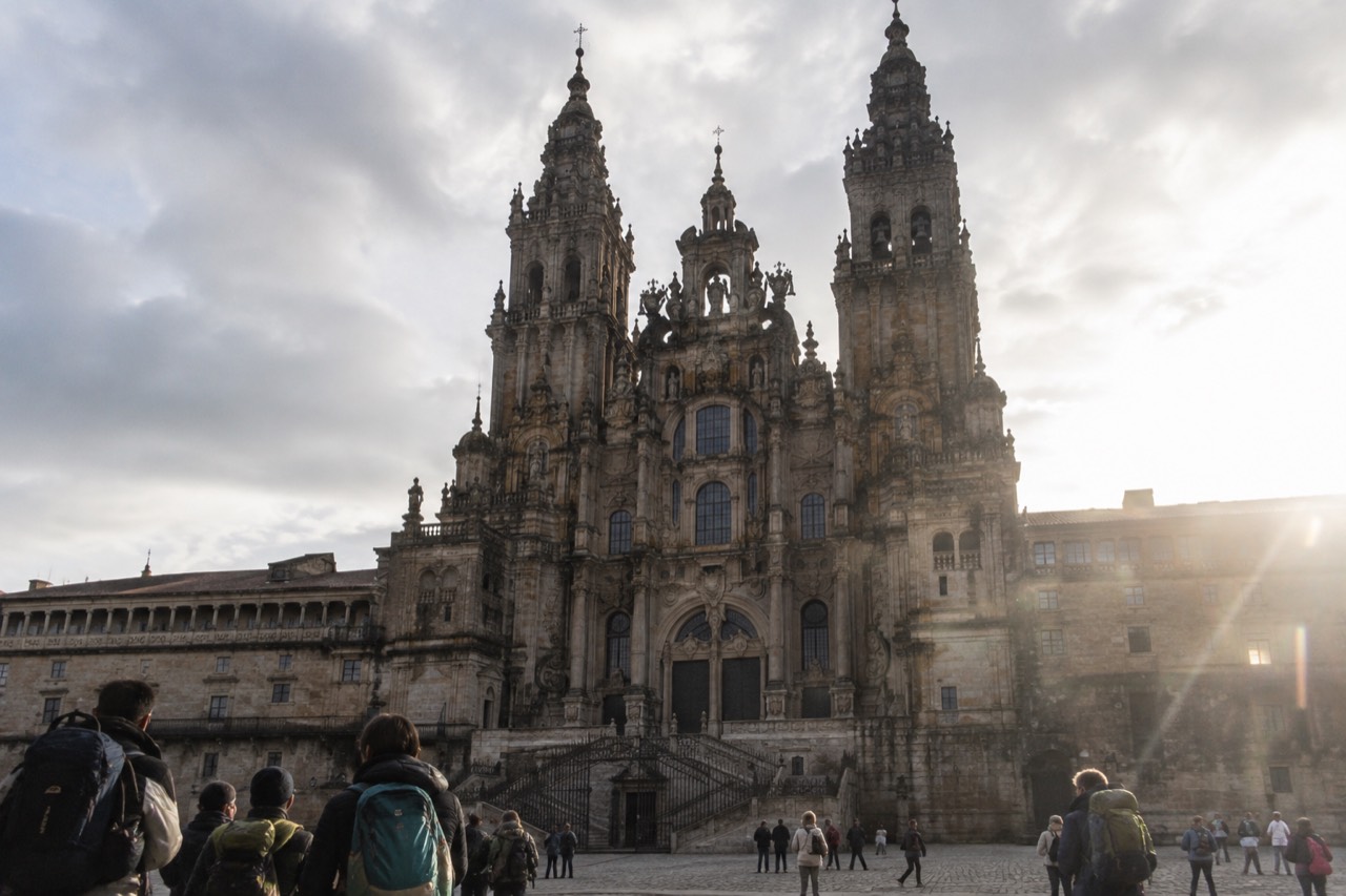 Pilgrims with backpacks waiting at a wooden counter inside a bright stone building in Santiago de Compostela