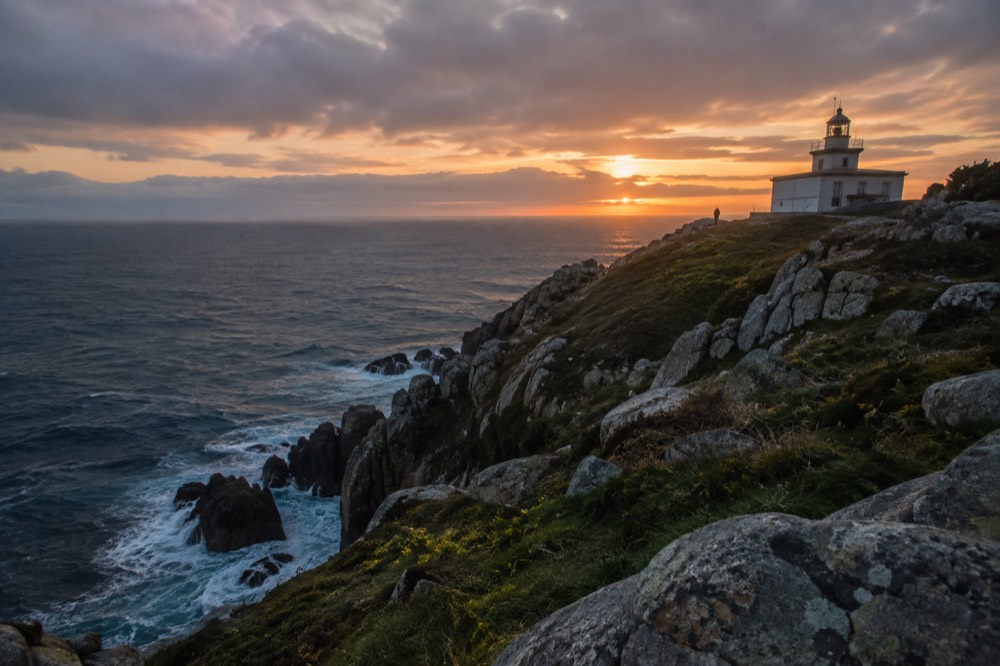A rocky Atlantic headland at sunset with a lighthouse on the Costa da Morte near Fisterra
