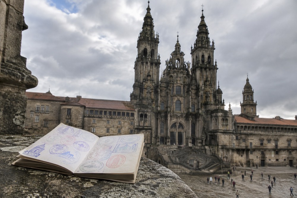 A finished credencial resting on a stone parapet with the towers of Santiago de Compostela Cathedral rising behind it