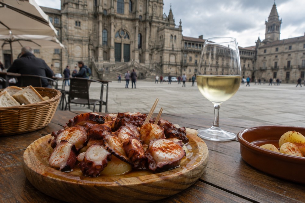 A bowl of Galician pulpo a la gallega with olive oil and paprika on a wooden table in a busy tapas bar