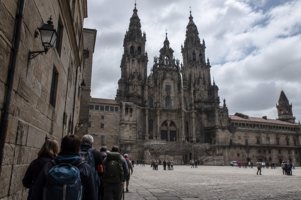 A queue of walkers with backpacks outside a stone building in an old Galician street