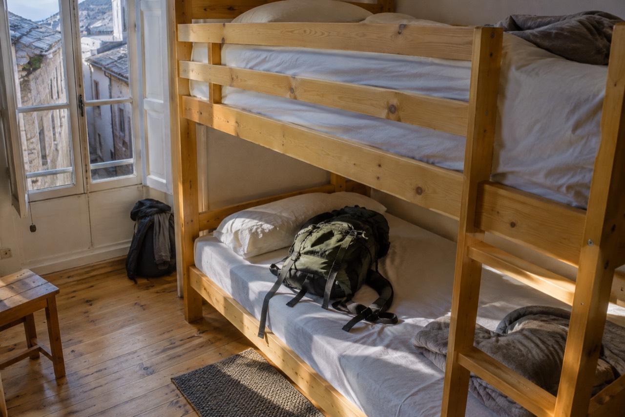 A bunk bed in a bright wooden hostel dorm room with a backpack resting on one mattress