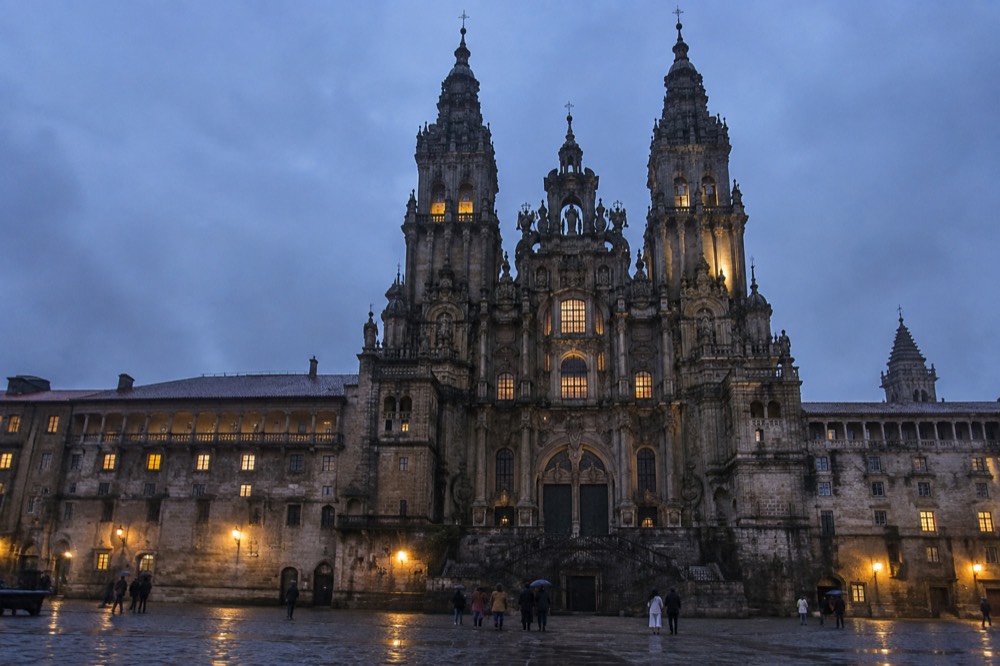 A rain-wet granite square at dusk with the Cathedral towers lit behind rooftops