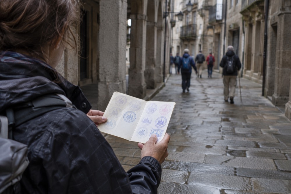 A pilgrim holding a credential passport open to show a row of ink stamps