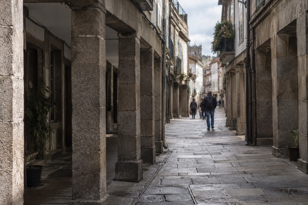 A narrow granite street in the old town of Santiago de Compostela with stone arcades and hanging signs