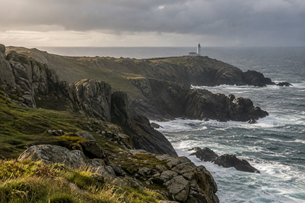 A lighthouse on green sea cliffs at the western end of the Costa da Morte coastline